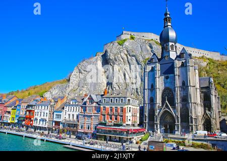 Dinant, Belgien - März 9. 2022: Blick über die gotische Kirche, Felswand auf der Uferpromenade des Flusses meuse mit Cafés und Restaurants Stockfoto