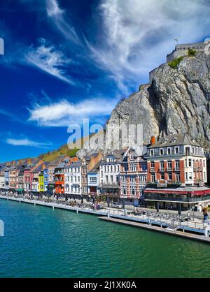 Dinant, Belgien - März 9. 2022: Blick auf die Uferpromenade Bunte Häuser gegen steile Felswand, beeindruckend blauer Himmel Stockfoto