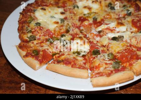 Eine große Pizza auf einem weißen Teller als Teil einer Mahlzeit. Stockfoto