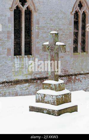 Ein Steinkreuz kennzeichnet den Ort einer Bestattung auf dem Friedhof von Schnee bedeckt. der Kirchhof ist ein ziemlich reflektierenden Ort gemacht durch die dicken Abdeckung der Schnee noch friedlich. Stockfoto