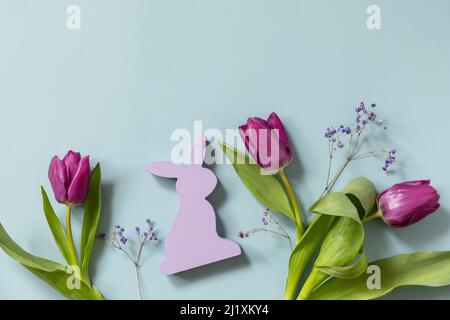 Lila Tulpen mit lila Kaninchen auf blauem Hintergrund. Konzept für Frühlings- und Osterferien. Draufsicht flach liegend. Speicherplatz kopieren. Stockfoto