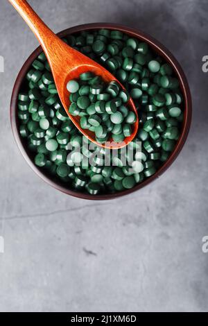 Vitamine aus Spirulina in einem Holzbecher mit einem Holzlöffel auf dunklem Hintergrund. Vegetarische Quelle von Aminosäuren und Omega 3 Stockfoto