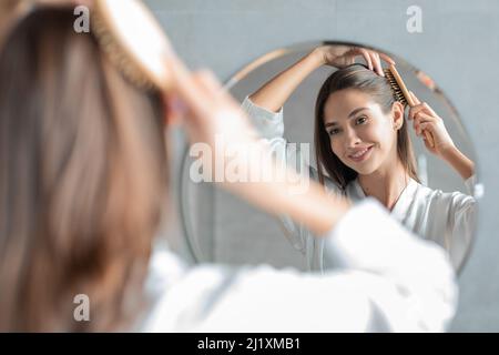 Junge Attraktive Dame Kämmt Ihr Haar Mit Pinsel Und Blick Auf Spiegel Stockfoto