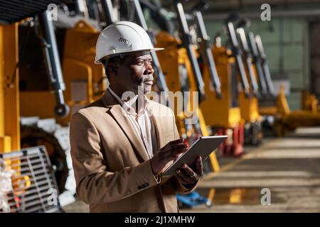 African Engineer in Work Helm mit digitalen Tablet, um die Logistik in der Fabrik zu steuern Stockfoto