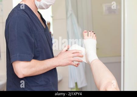 Der Arzt verband das Bein des Patienten. Chirurg und Patient nach Venenoperation. Stockfoto