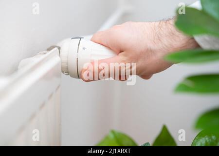 Man Hand regelt den Temperaturregler des Heizkörpers, um die Heizkosten zu senken. Stockfoto