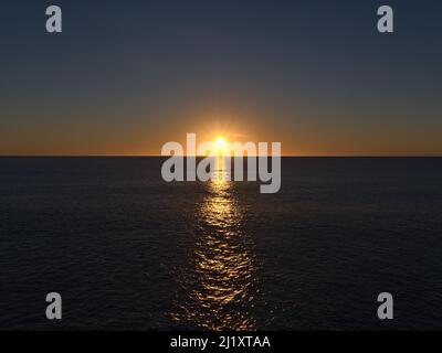 Atemberaubender Sonnenuntergang mit strahlender Sonne am Horizont über dem Atlantischen Ozean von Playa de Amadores in Puerto Rico, im Süden von Gran Canaria, Spanien. Stockfoto