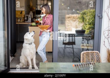 Frau steht mit ihrem entzückenden weißen Hund auf der Terrasse zu Hause zusammen Stockfoto