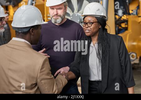 Geschäftspartner in Arbeitshelmen begrüßen sich gegenseitig und schütteln sich die Hände während des Meetings im Werk Stockfoto