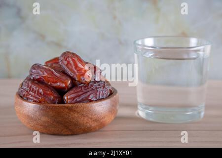 Glas Wasser mit einer Schale Datteln Obst auf einem hölzernen Hintergrund.Muslime brechen das Fasten mit Wasser und Datteln Stockfoto