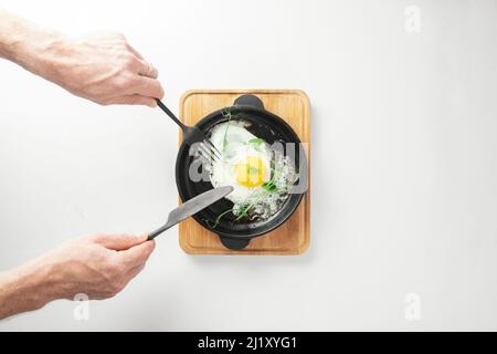 Servieren von Spiegeleiern in gusseiserner Pfanne mikrogrüne Sprossen Baby Bohnen Erbse und Sonnenblume auf weißem Hintergrund, Draufsicht. Stockfoto