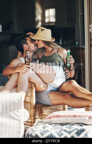 Sie sind jung und verliebt. Kurzer Schuss eines liebevollen jungen Paares, das sich küsst, während es auf der Terrasse ein paar Biere genießt. Stockfoto