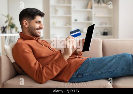 Lächelnder Mann mit Tablet und Kreditkarte, der auf der Couch sitzt Stockfoto