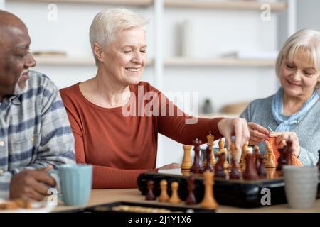 Attarctive ältere Frau, die mit multirassischen Freunden Schach spielt Stockfoto