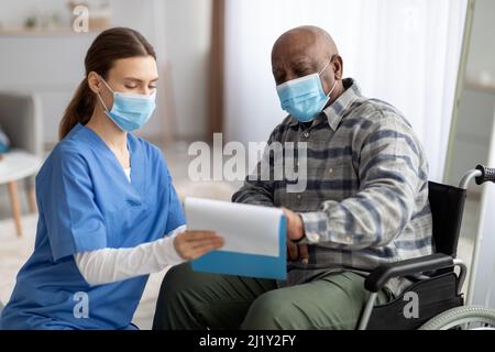 Frau in Arbeitskleidung hilft schwarzen älteren Mann füllen Papiere Stockfoto