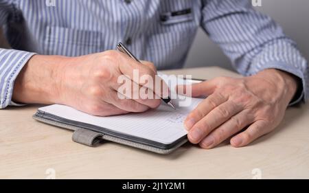 Mann Hände Nahaufnahme Notizen im Planer. Schüler oder Mitarbeiter schreiben Pläne, Gedanken, Erinnerungen, wichtige Informationen in Notizbücher. Hochwertige Fotos Stockfoto