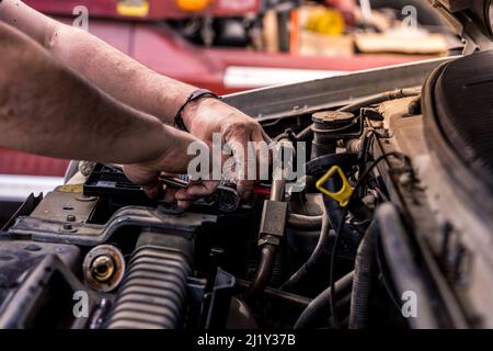 Mechaniker mit schmutzigen Händen arbeitet am Automotor. Authentische Aufnahme eines echten Automechanikers, der am Motor arbeitet. Stockfoto