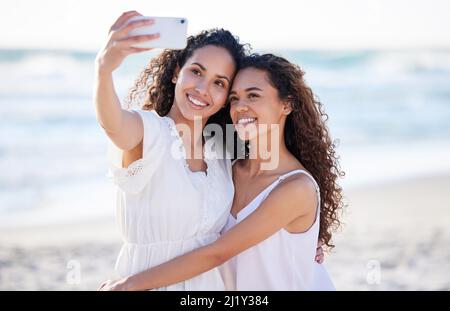 Wie glücklich bin ich, sie in meinem Leben zu haben. Aufnahme von zwei jungen Frauen, die am Strand Selfies machen. Stockfoto