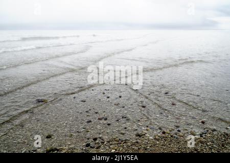 Überlappende, sich schneidende Wellen an der mit Nebel bedeckten Küste mit dramatisch bewölktem Himmel. Natürlicher trübe Hintergrund, Muster, Textur von Wasser. Interferenc Stockfoto