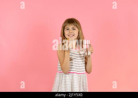 Ein kleines Mädchen auf einem rosa Hintergrund nimmt Fischöl. Ein Kind hält eine Omega-3-Kapsel in den Händen. Ein kleines Mädchen lächelt fröhlich während der Einnahme von Omega 3 Stockfoto