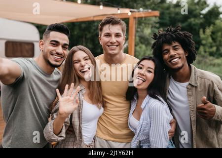 Glückliche, vielfältige junge Freunde posieren in der Nähe von Wohnmobil, Spaß haben, albern sein, zeigen verschiedene Gesten auf Campingausflug Stockfoto