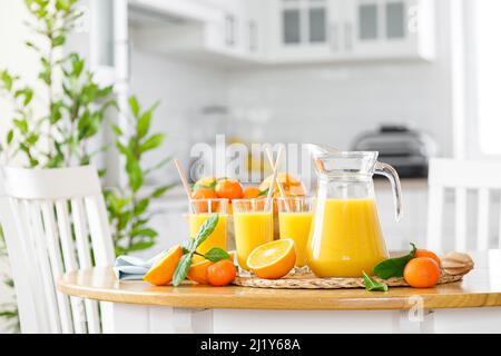 Frisch gepresster Orangensaft in einem Glaskrug, Gläser und frisches Obst mit Blättern auf dem Tisch vor dem Hintergrund der modernen weißen Küche, Gesundheit Stockfoto