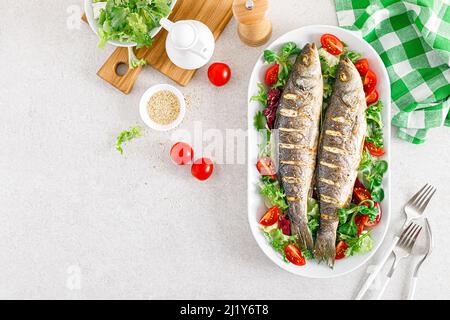 Seebarsch oder Seebarsch Fisch geröstet und frisches Gemüse Salat aus Tomaten und Salat, gesunde Ernährung zum Mittagessen, Draufsicht Stockfoto