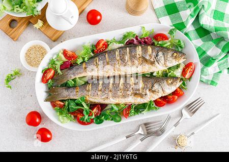 Seebarsch oder Seebarsch Fisch geröstet und frisches Gemüse Salat aus Tomaten und Salat, gesunde Ernährung zum Mittagessen, Draufsicht Stockfoto