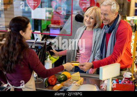 Lächelnder älterer Mann, der im Supermarkt mit Kreditkarte bezahlt Stockfoto