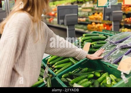 Frau pflücken frische lange Gurken in einem Einkaufswagen auf dem Lebensmittelmarkt. Stockfoto