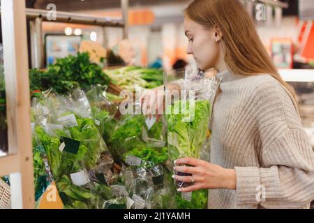 Nahaufnahme Porträt, hübsche junge Frau in Pullover Abholung, Auswahl Microgreens Verpackung im Lebensmittelgeschäft Stockfoto