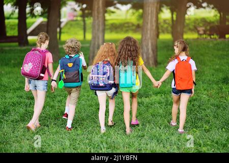 Gruppe von Kindern mit Schulrucksäcken, die Hand in Hand gehen. Ferien, zurück zur Schule, Sommerlager. Stockfoto