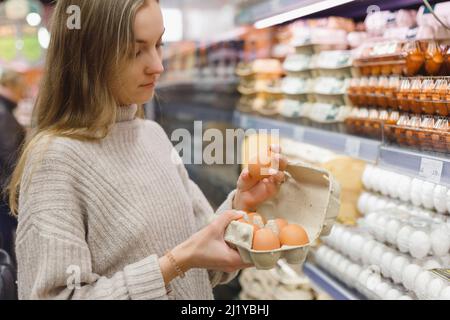 Frau wählt Hühnereier in einem Lebensmittelgeschäft. Nahrungsaufnahme, Ostern. Stockfoto