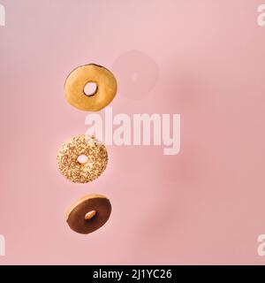 Fallende leckere Donuts mit Schokolade, Vanille und Streuseln bedeckt, auf minimalem rosa Pastell Hintergrund mit Platz für Kopie Platz. Stockfoto