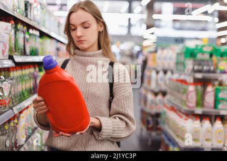 Die junge Frau wählt Waschmittel und Conditioner oder ein Waschgel in einem Geschäft Stockfoto