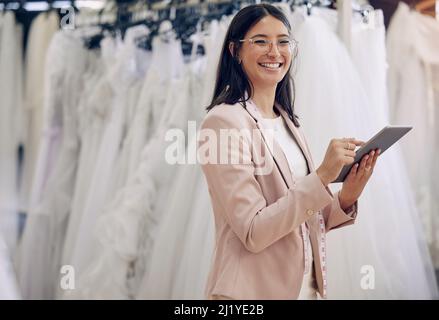 Sie können unsere Kleider online oder im Geschäft durchsuchen. Aufnahme einer Näherin mit einem digitalen Tablet während der Arbeit in einer Boutique. Stockfoto