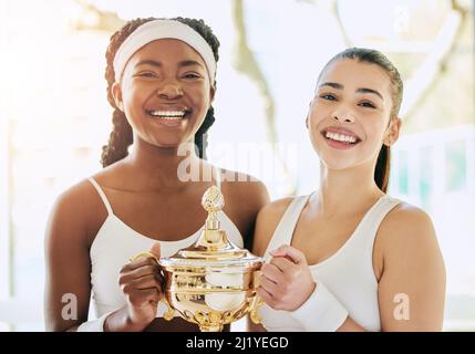 Doppel-Champions. Beschnittenes Porträt zweier attraktiver junger Tennisspielerinnen, die während ihres Awards im Clubhaus eine Trophäe halten Stockfoto