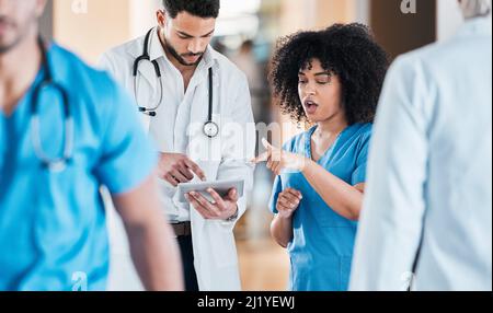 Die Telemedizin wie die Profis zu nutzen. Aufnahme von zwei jungen Ärzten, die ein Tablet benutzen und in einem modernen Büro diskutieren. Stockfoto