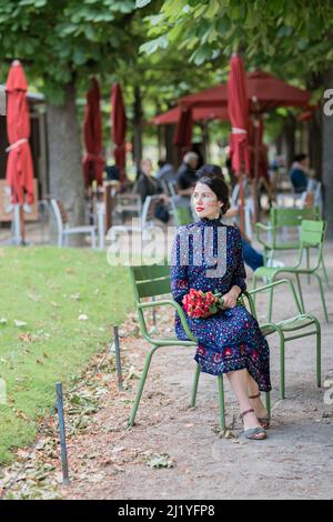 Hübsche Frau in einem dunkelblauen Kleid, die auf einem Stuhl im Park sitzt Stockfoto