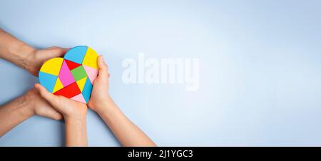 Konzept des Welt-Autismus-Tages. Erwachsene und Kinder Hände halten Puzzle Herz auf hellblauem Hintergrund. Draufsicht Stockfoto
