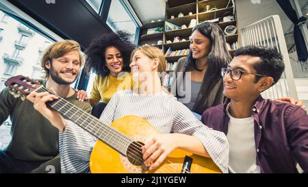 Gruppe von fünf multirassischen jungen Menschen in lässigen Kleidern singen und spielen Musik in Innenräumen, junge Freunde, die Spaß haben und Zeit miteinander verbringen, Millenn Stockfoto