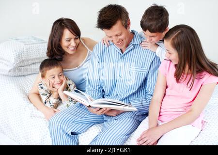 Es gibt nichts Wichtigeres als eine gute Zeit zusammen. Eine liebevolle fünfköpfige Familie liest zusammen auf einem Bett. Stockfoto