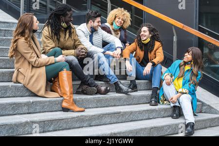 Eine Gruppe von Freunden, die im Freien sitzen und reden, Leute mit Gesichtsmaske, sozialer Distanz und Treffpunkt im Freien Stockfoto