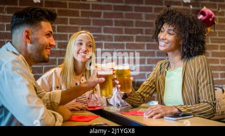 Eine Gruppe von Freunden jubelt mit Bier und hat Spaß in einem Pub, multikulturelle Leute haongout Stockfoto