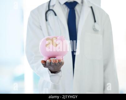 Brauchen Sie eine Schuldenberatung Besuchen Sie unsere Geldklinik. Aufnahme eines nicht erkennbaren Arztes, der ein Sparschwein mit einem Pfand hält, der es bedeckt. Stockfoto