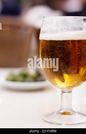 Bier im Glas auf einem Tisch im Freien mit Oliven im Hintergrund Stockfoto