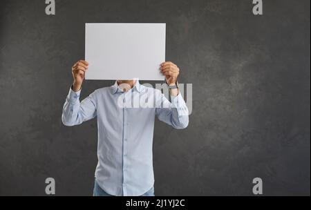 Mann, der ein weißes Blatt Papier vor seinem Gesicht hält, das Platz für Kopien auf der Kamera zeigt. Stockfoto