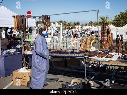 Afrikanischer Verkäufer in traditioneller Kleidung, der am 13. März 2022 auf dem Sonntagsmarkt in Teguise auf Lanzarote, Spanien, geschnitzte Holzmasken verkauft Stockfoto