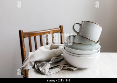Eine Pyramide aus weißen Schalen, Tellern und Tassen in verschiedenen Größen und Farben auf einem beigen Tisch in der Küche. Skandinavischer Stil. Ort für Ihren Text. Kopieren Stockfoto