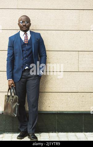 Porträt eines dunkelhäutigen afroamerikanischen Geschäftsmannes in Anzug im Freien, der vor dem Hintergrund einer Gebäudewand posiert Stockfoto